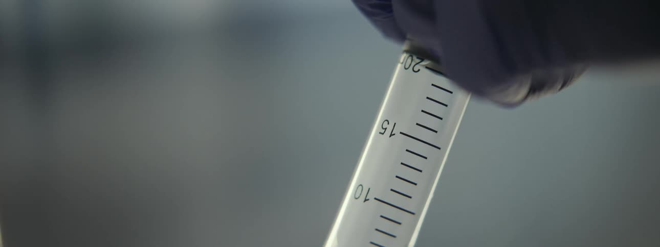A close-up view of a gloved hand slowly filling a syringe with clear liquid in a sterile environment