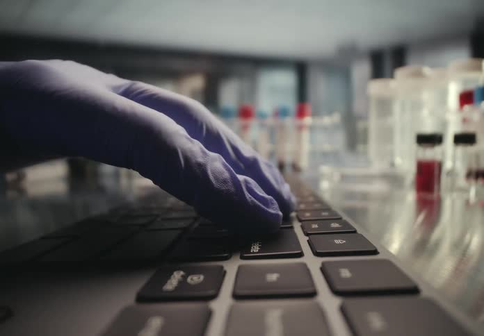 A researcher wearing gloves types on a laptop keyboard with blood samples in a laboratory