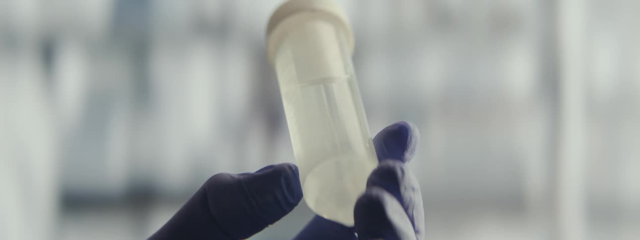 A scientist in a sterile lab gently swirls a clear liquid inside a plastic test tube