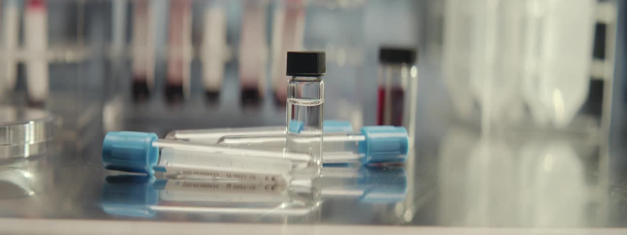Close up on medical test tubes and vials with clear and red liquid on a reflective countertop in a laboratory