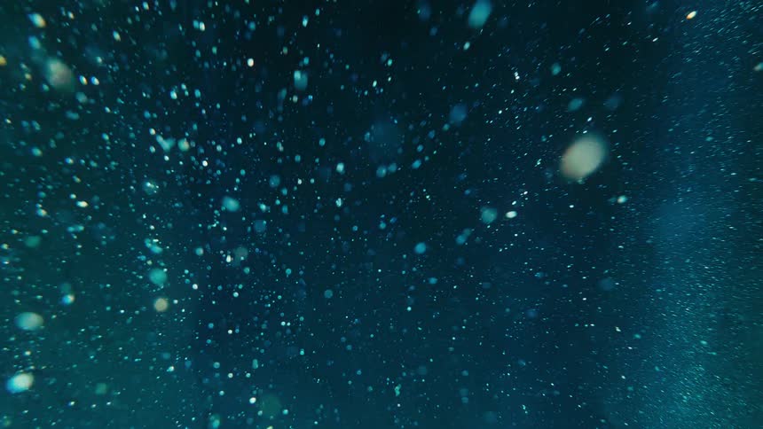 Abstract shot of shimmering particles floating and drifting through a dark blue space