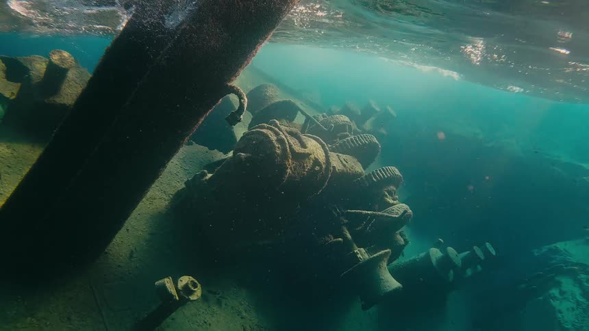 Close-up of the rusty engine of a shipwreck submerged in clear turquoise water with sunlight beams