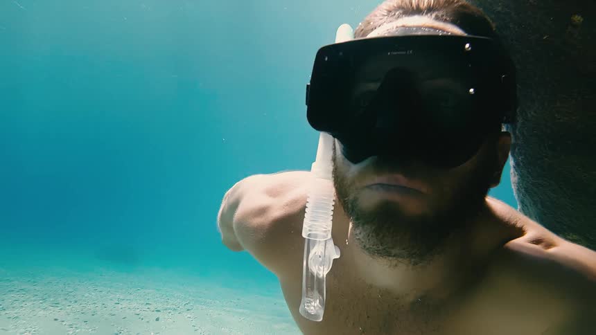 An intense underwater portrait of a man in a snorkel mask looking directly at the camera