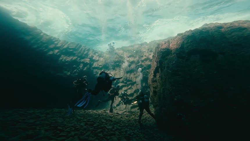 Low-angle view of a group of scuba divers exploring a beautiful underwater rock cavern
