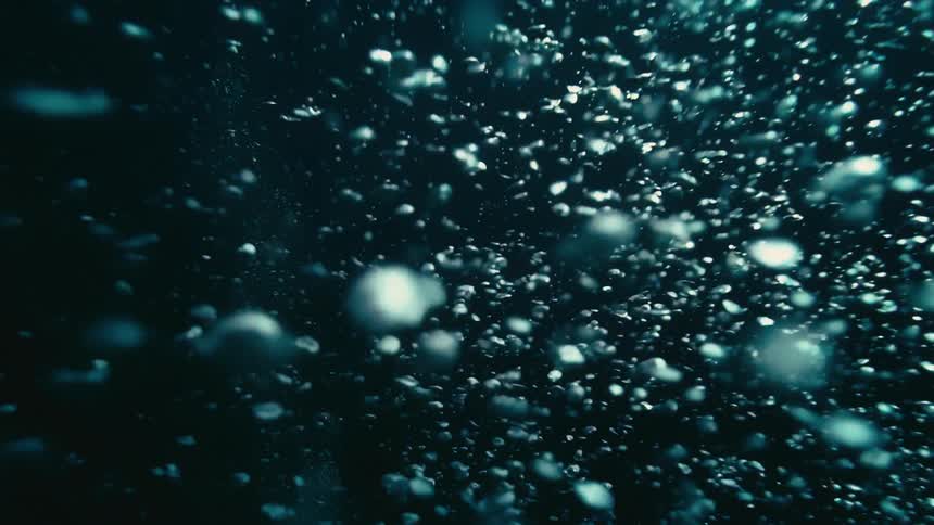 Countless air bubbles slowly ascend through the dark, deep water in an abstract underwater view