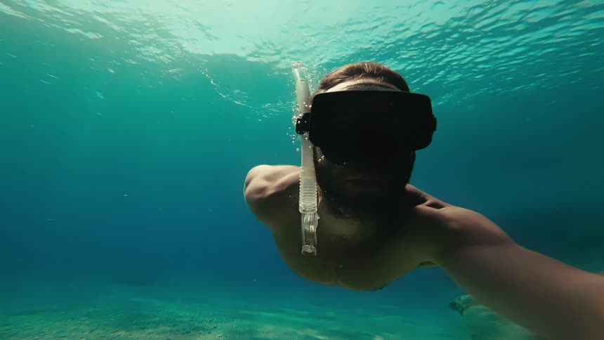 Slow motion underwater selfie of a man snorkeling in the clear turquoise ocean with sunlight filtering through the surface
