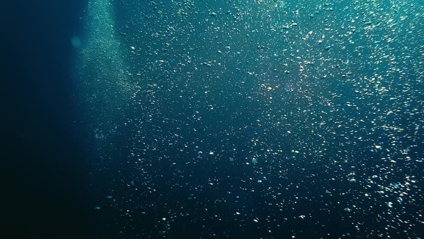 Serene underwater view of a myriad of air bubbles ascending in slow motion through the deep blue water