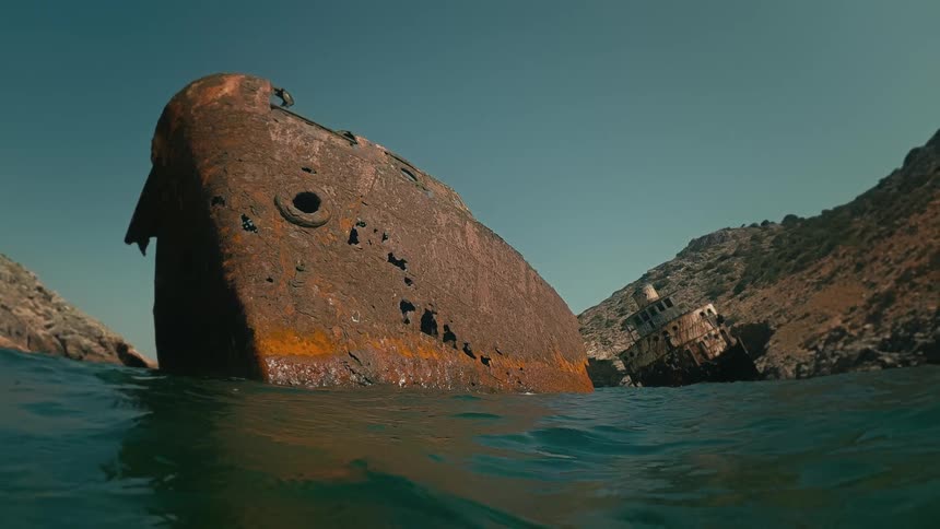 A dramatic water-level view shows a large, rusted shipwreck in a bay before the camera dips below the surface
