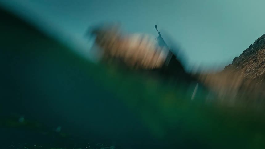 A split-level underwater view of a large rusty shipwreck half-submerged against a rocky coast