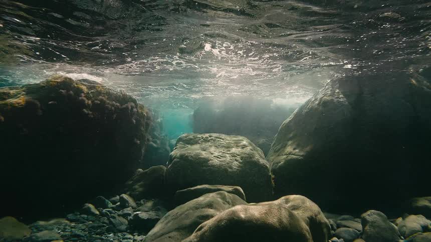A serene underwater view from a rocky riverbed as sunlight filters through the turbulent surface