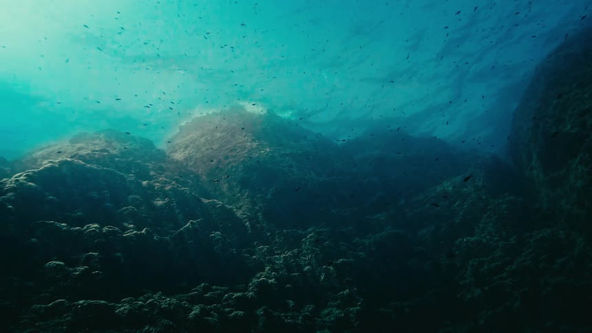Sunbeams pierce the turquoise water, revealing a tranquil and mysterious underwater valley of moss-covered rocks