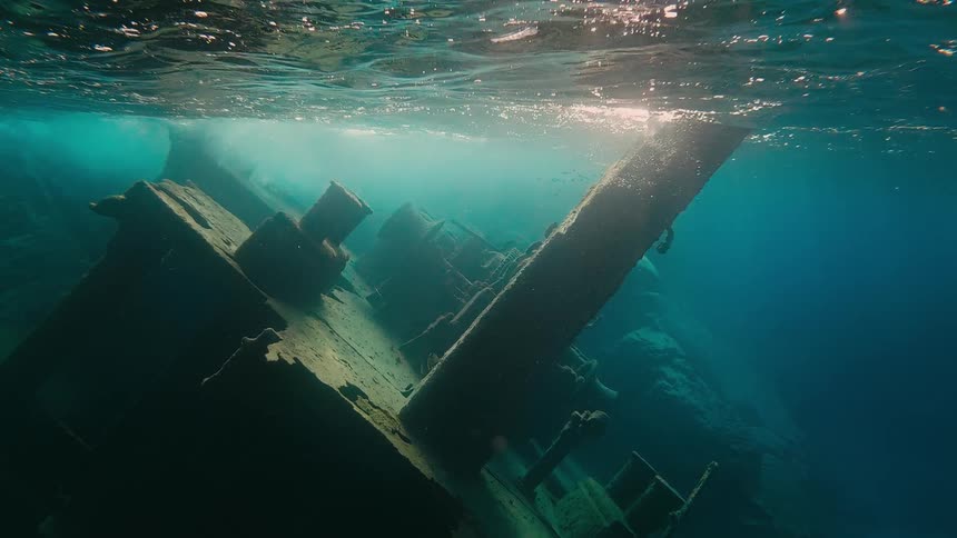 A sunken shipwreck rests on the seabed as sunlight penetrates the clear turquoise water from above