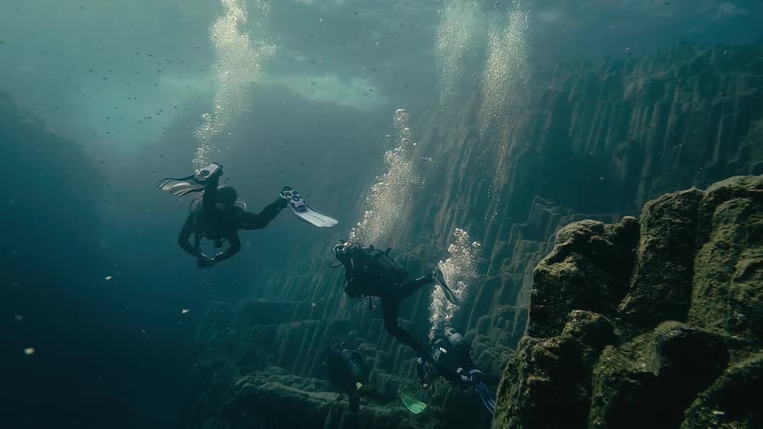A team of scuba divers explores a mysterious deep underwater canyon with unique terraced rock formations
