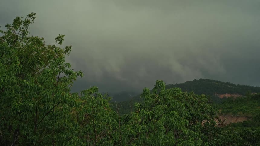 Ominous storm clouds roll over a lush, green mountain landscape on an overcast day