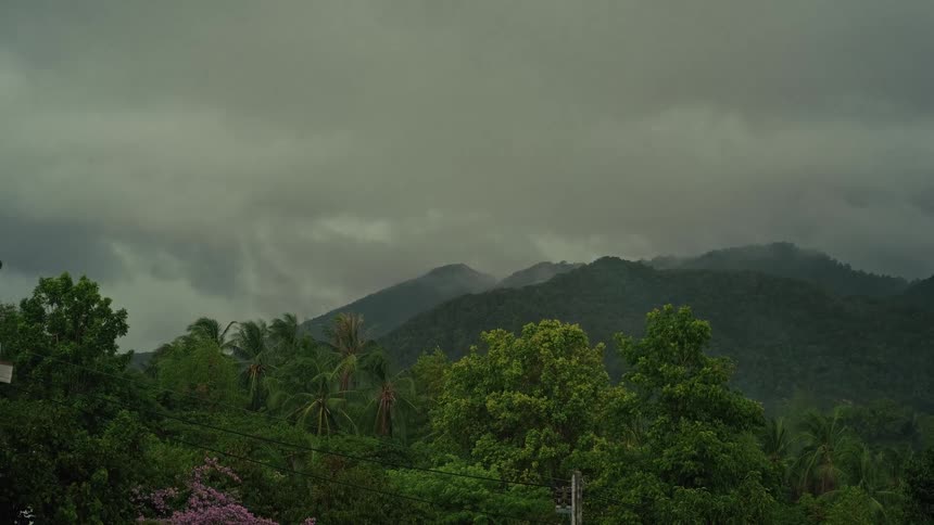 Heavy storm clouds move across the sky above a lush green jungle and mountains on a rainy day