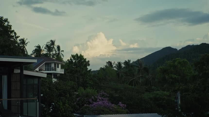 Modern homes are nestled amongst the trees of a lush, tropical hillside with mountains in the background