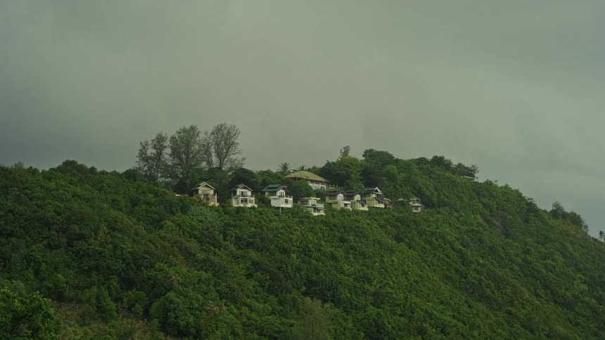 Gloomy, overcast sky hangs over a small village on a verdant tropical hillside