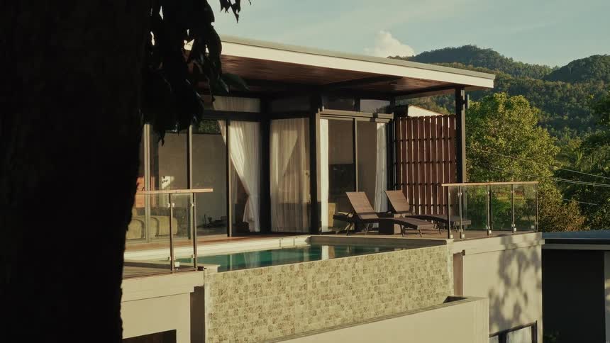 A luxury villa with a private pool and lounge chairs on a terrace overlooking a lush mountain landscape at golden hour