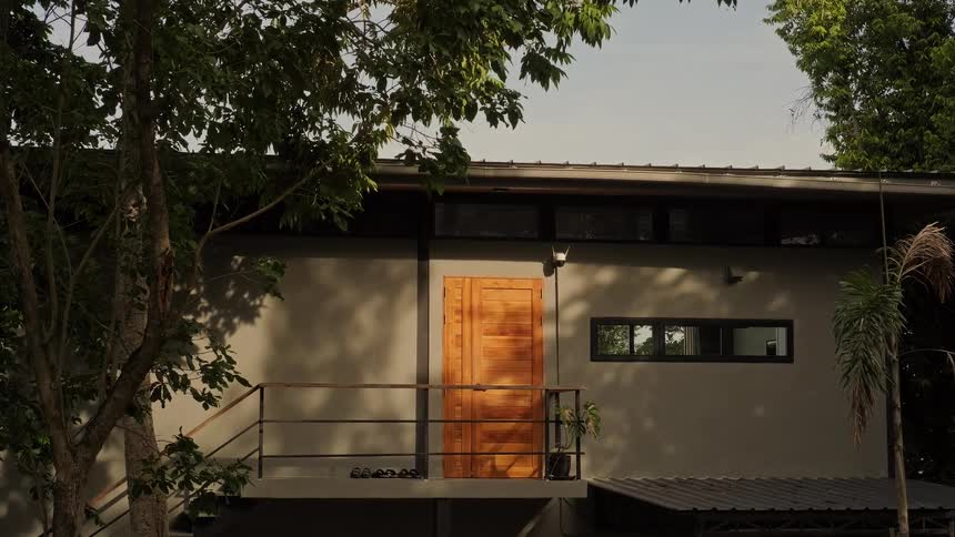 Sunlight casts shadows on the exterior of a modern, grey home with a wooden door, nestled among green trees