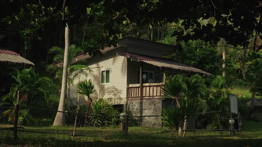 A tranquil bungalow is nestled in a lush, tropical jungle with dappled sunlight filtering through the trees