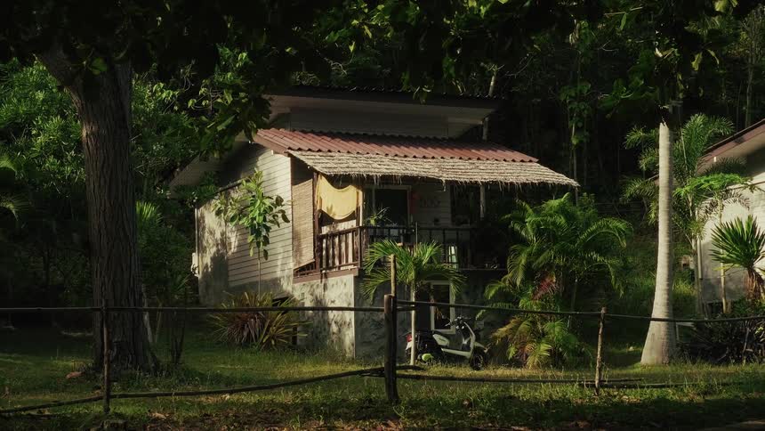 A secluded tropical bungalow is nestled amongst lush green jungle foliage with sunlight filtering through the trees