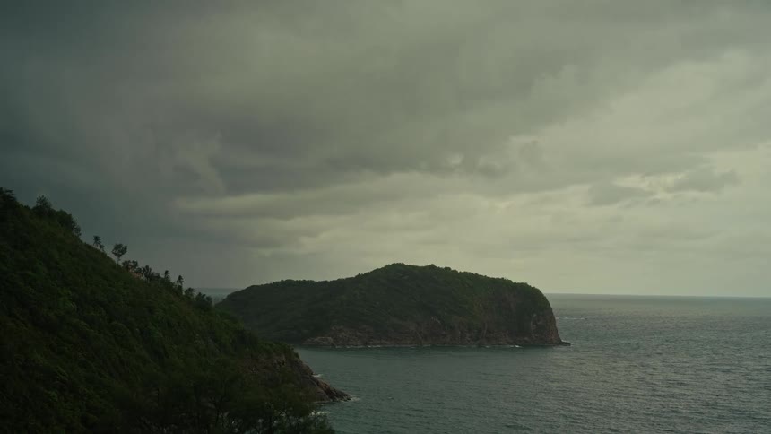A dramatic view of a tropical island under dark storm clouds as a storm approaches the coast