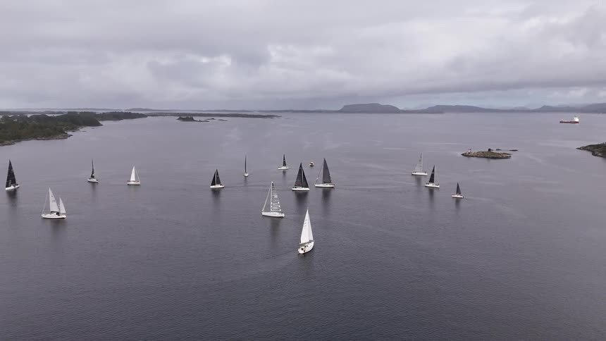 An aerial view of a fleet of sailboats competing in a regatta on a moody, overcast day
