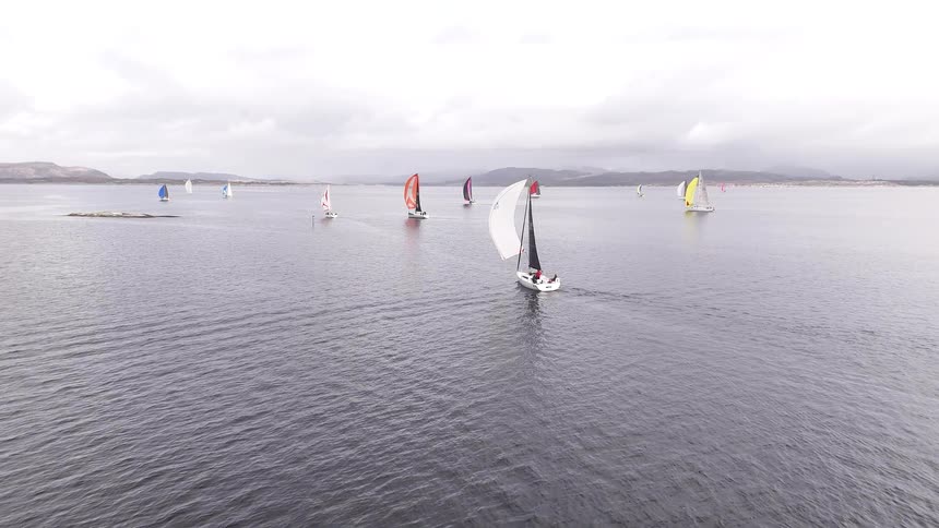 Aerial view of a fleet of sailboats with colorful spinnakers competing in a regatta on the open sea under an overcast sky