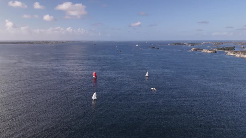 Sailboats with white and red sails glide across the calm blue sea during a summer regatta in a beautiful archipelago