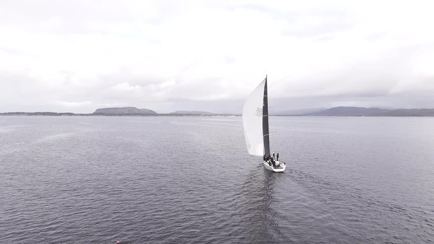 Aerial view of a sailboat with its spinnaker sail catching the wind as it travels across the calm ocean on an overcast day