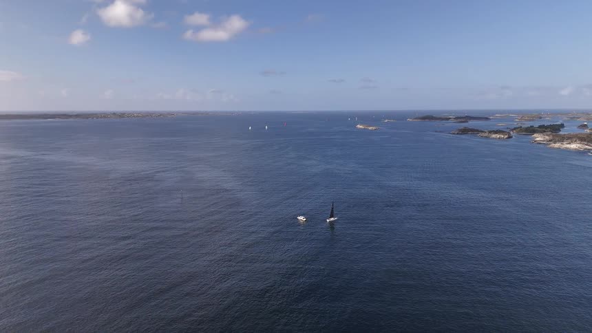 An expansive aerial view shows sailboats peacefully floating on the deep blue water of an archipelago on a beautiful day