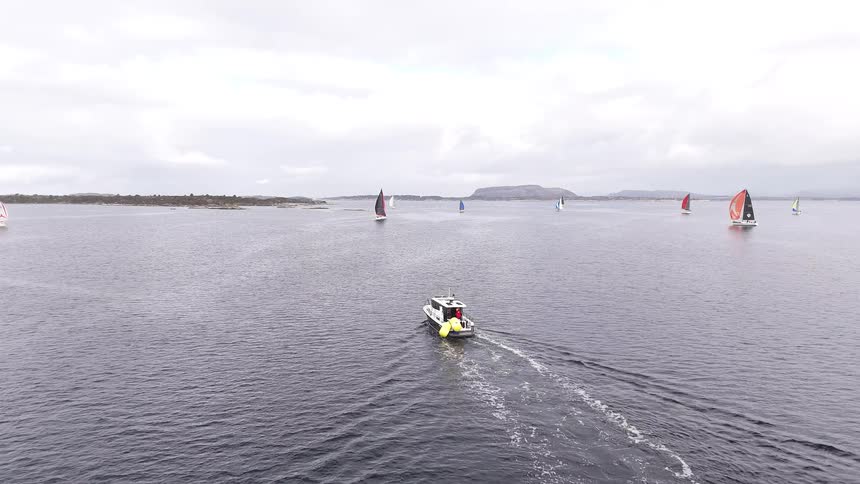 Aerial view of a motorboat and several sailboats scattered across a large body of water on a cloudy day
