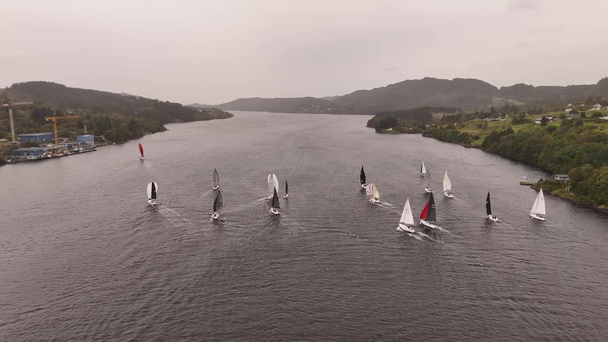A beautiful aerial view captures a fleet of sailboats competing in a regatta on a vast fjord on an overcast day