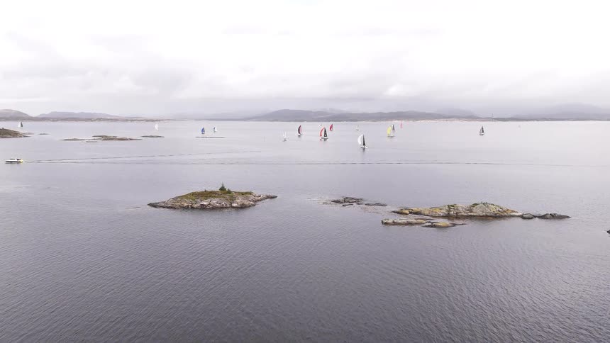 An aerial reveal shot of a sailing regatta behind a small forested island on a Scandinavian fjord