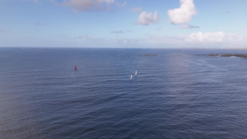 A serene and expansive view of sailboats dotting the calm blue ocean under a partly cloudy sky