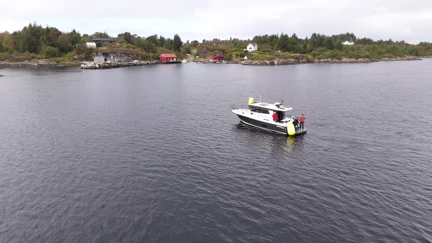 Aerial view of a modern motorboat with a crew floating on a calm fjord near a picturesque coastal village
