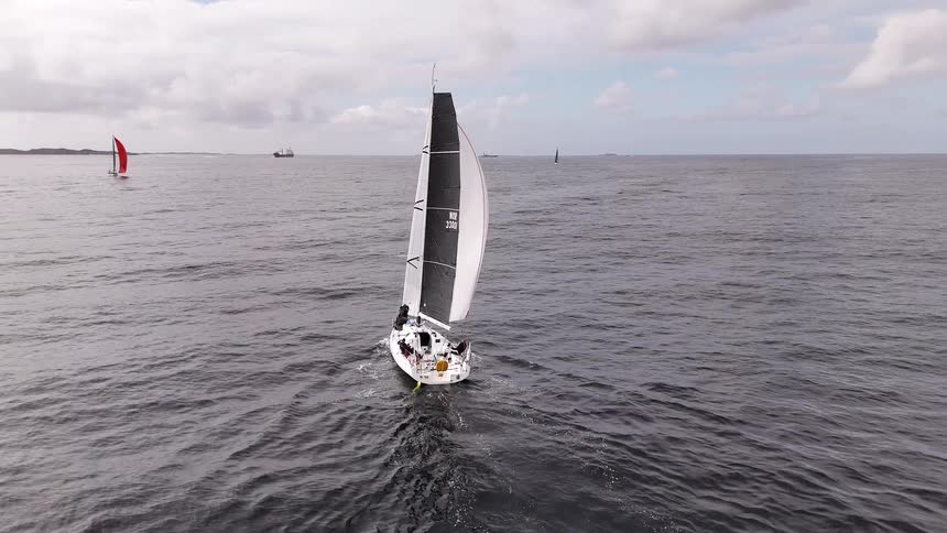 An aerial view follows a racing sailboat with a large spinnaker as it glides across the open ocean during a regatta