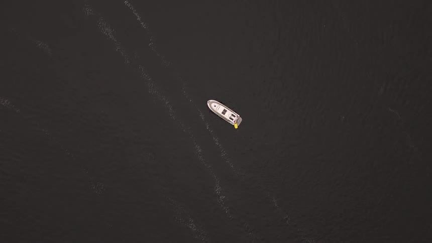 A serene aerial top-down view of a solitary white motorboat floating peacefully on the vast, dark water