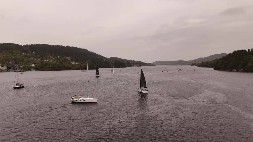 Aerial view of sailboats competing in a regatta on a wide fjord under an overcast sky