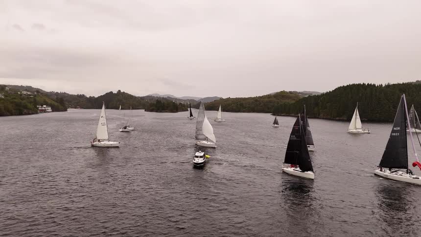 Aerial view of a fleet of sailboats competing in a regatta on a wide channel on an overcast day