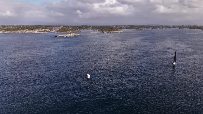 Sweeping aerial footage reveals boats navigating the vast, deep blue waters of a rugged Scandinavian archipelago under a cloudy sky