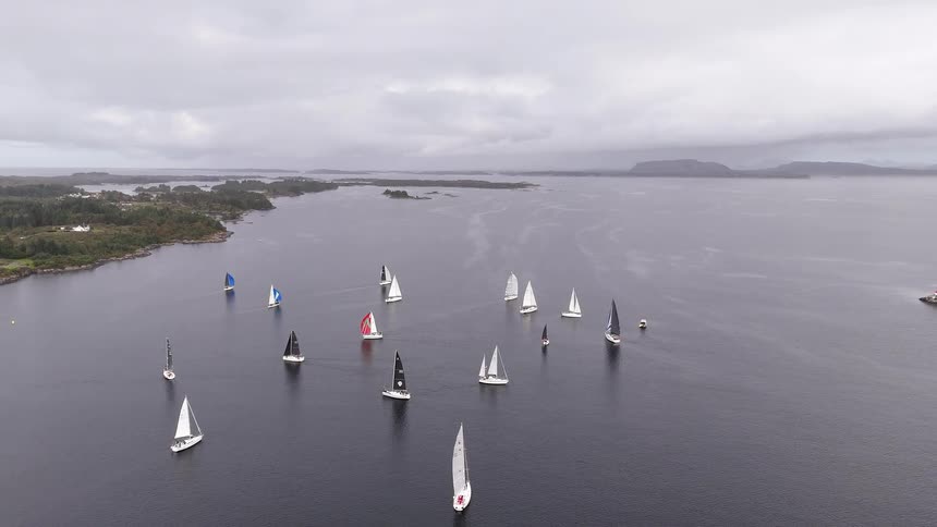 An epic aerial view captures a fleet of sailboats with colorful sails competing in a regatta on a vast fjord under a cloudy sky