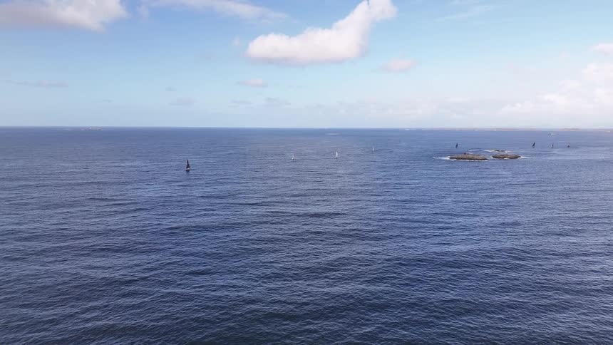 A serene wide aerial view of sailboats dotting the vast blue ocean on a calm day