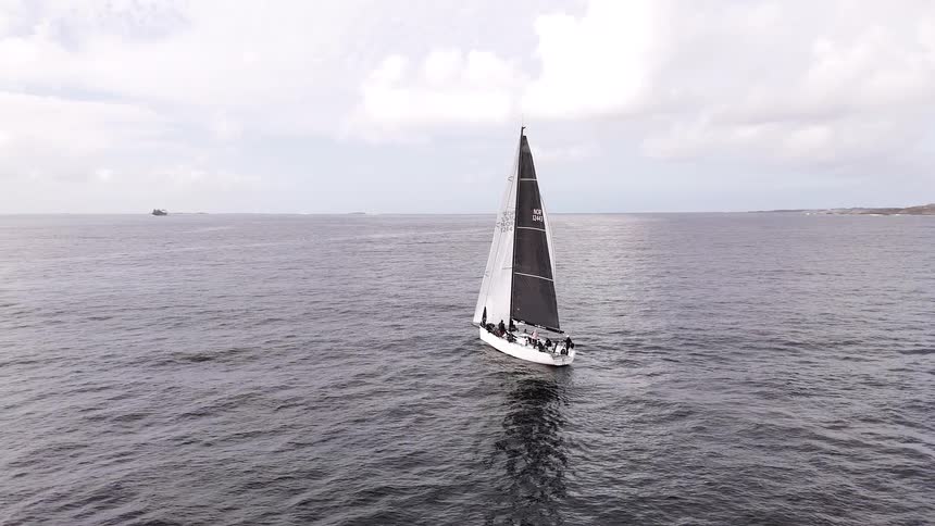 An epic aerial shot reveals a modern racing sailboat gliding across the vast open ocean under a cloudy sky