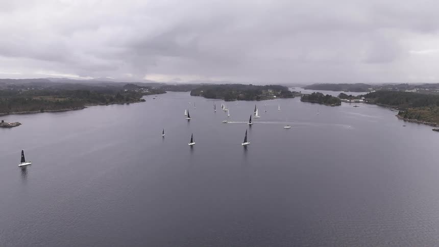 An expansive, static aerial view of a sailboat regatta on a vast fjord under an overcast sky
