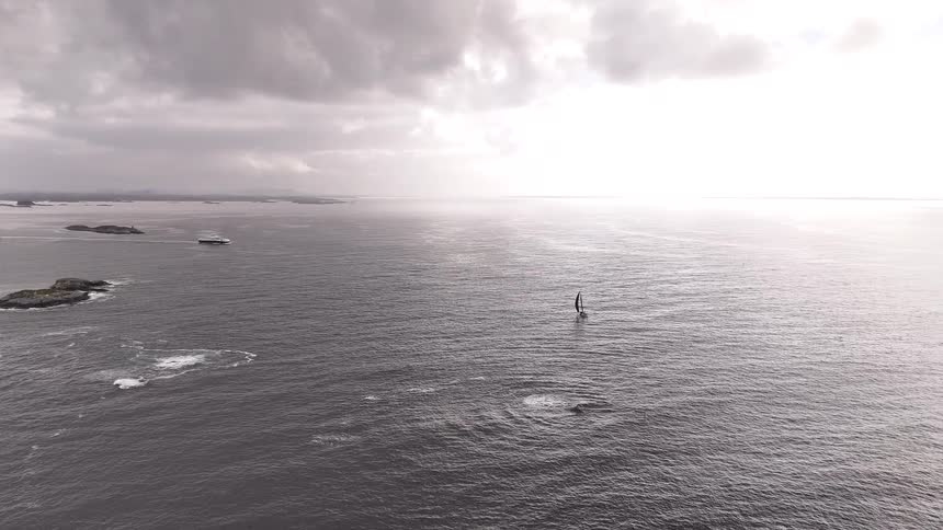 Dramatic aerial shot of a whale breaching near a lone sailboat on the open sea under an overcast sky