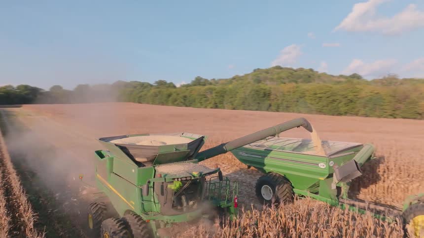 Aerial view of a combine harvester collecting corn and loading it into a tractor-trailer during a sunny day on a farm