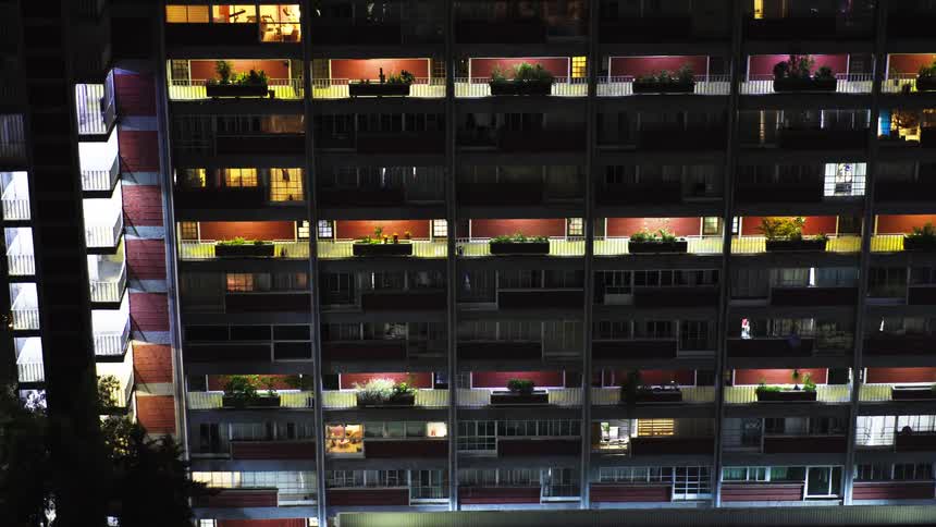 Time-lapse of a large, illuminated apartment building at night shows the comings and goings of residents