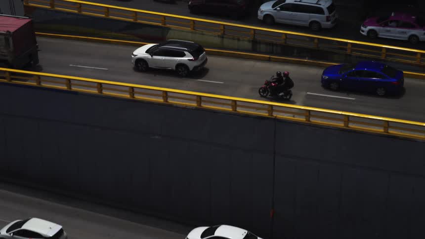 An overhead slow-motion view of cars, a truck, and a motorcycle navigating a congested city highway