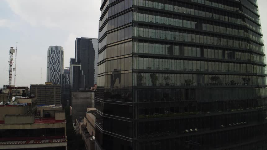 A slow reveal of a modern glass skyscraper and the surrounding cityscape on an overcast day